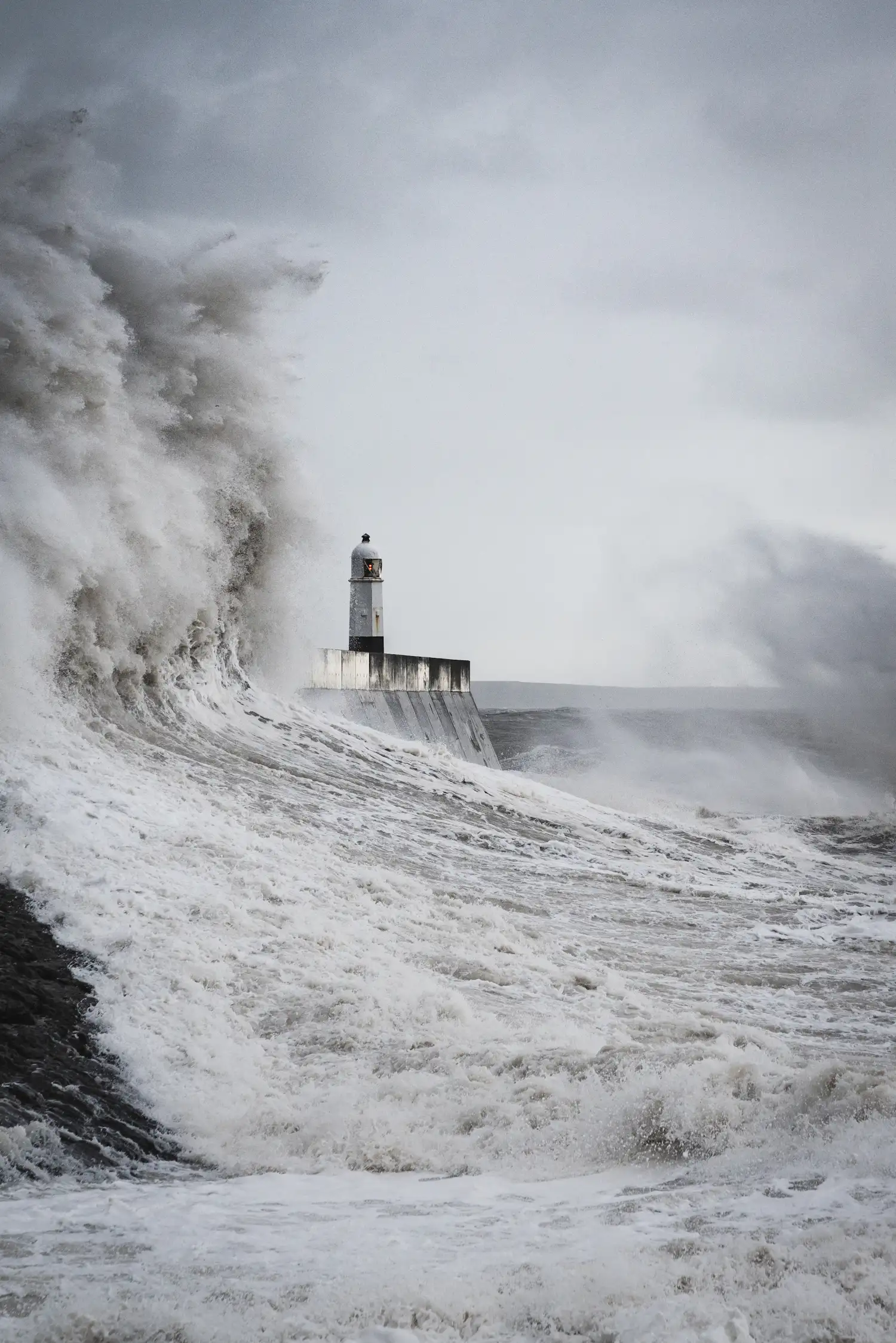 A wave towering over a harbour lighthouse