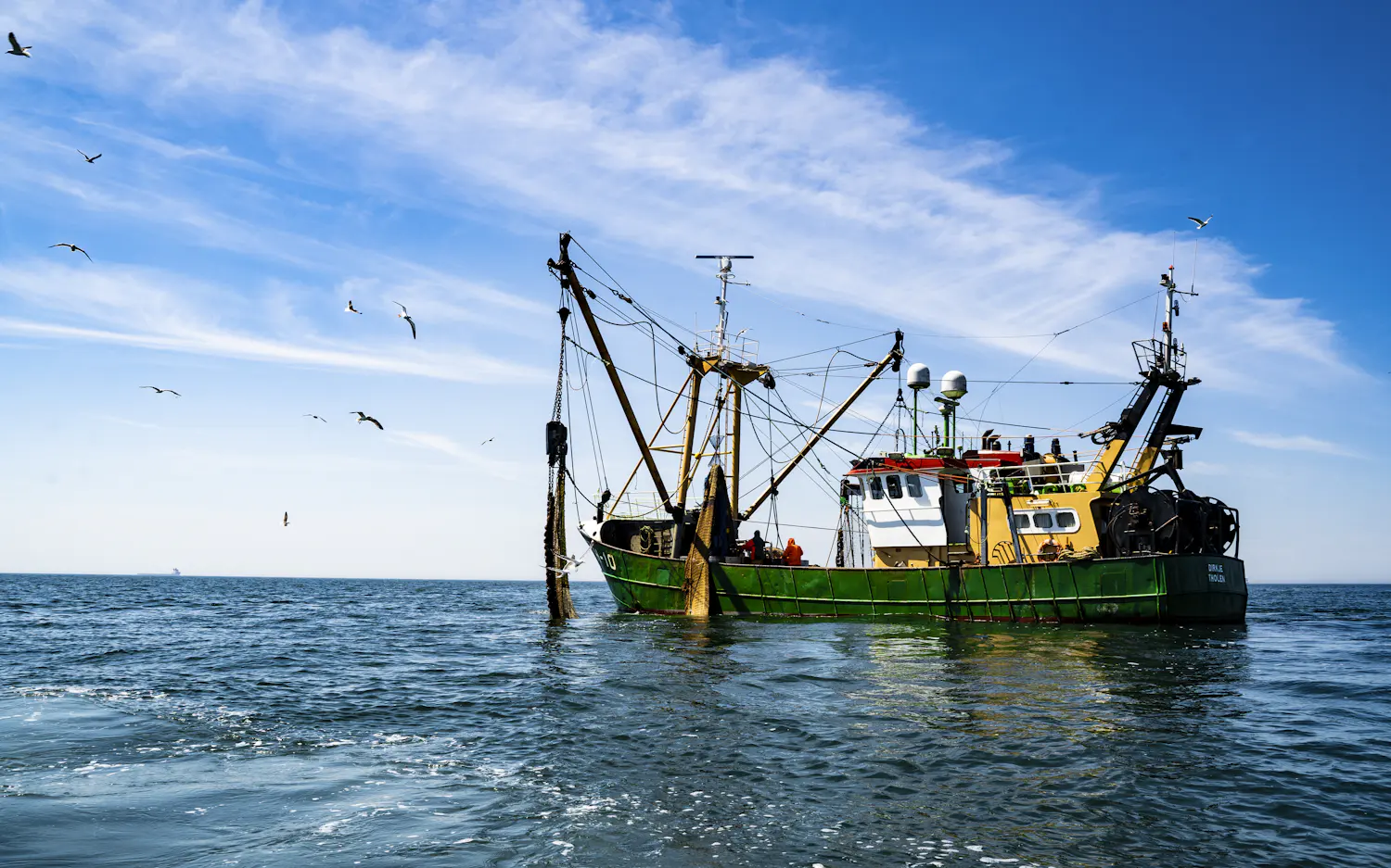 A green and yellow trawler heading out under a blue sky