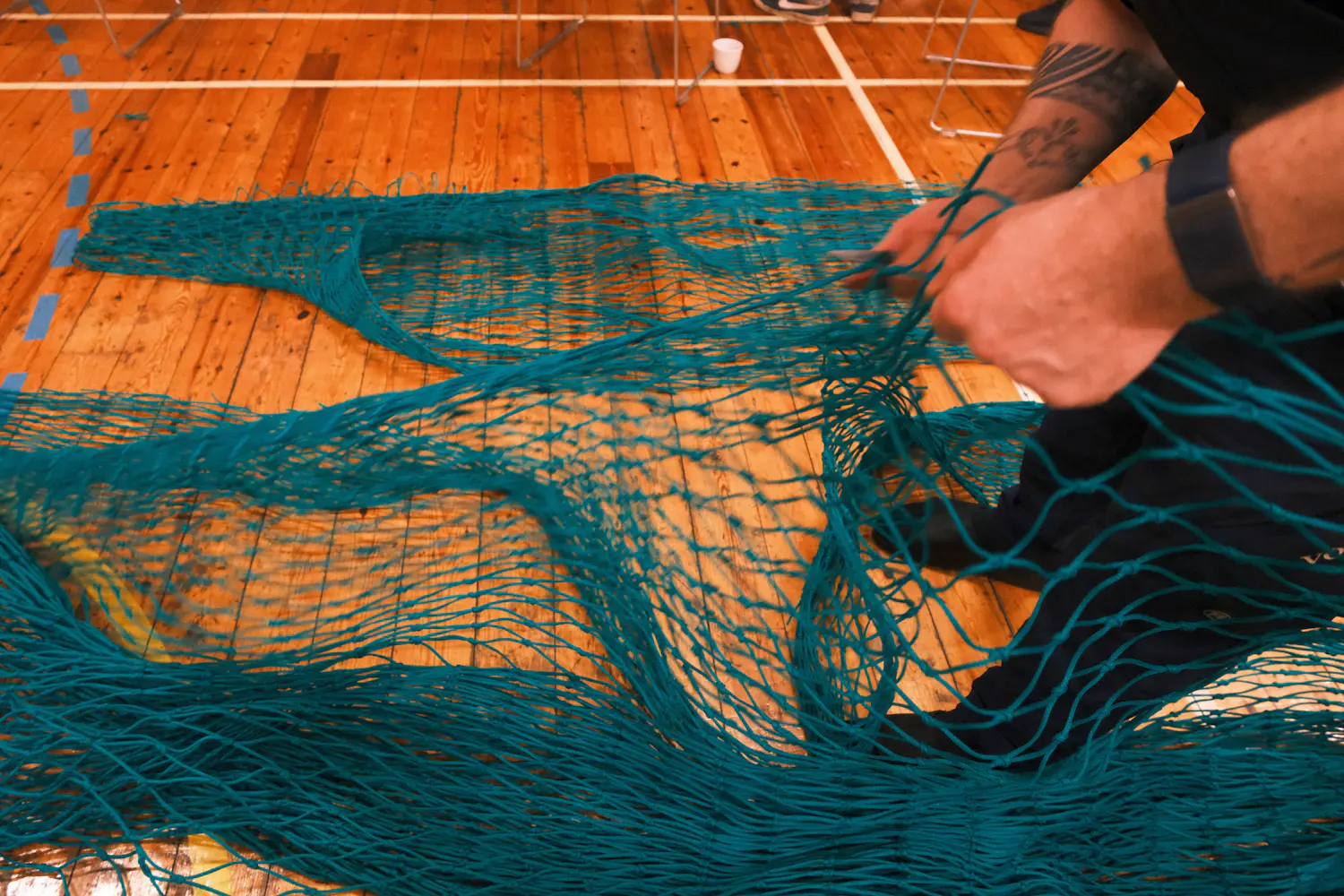 Green net spread across a wooden floor while hands work through it