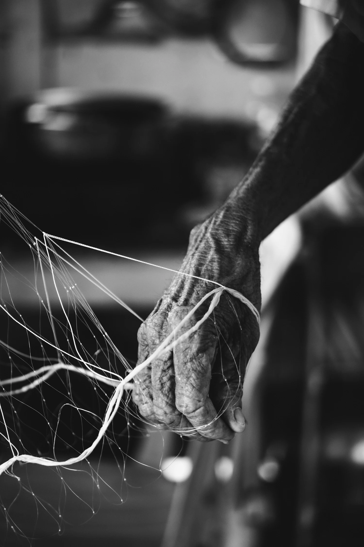 Weathered hands pulling fine net twine taut, in black and white