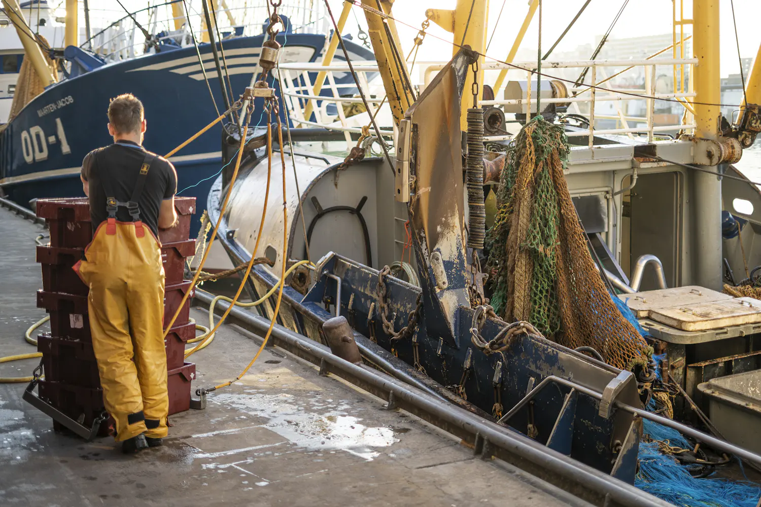 A crewman in yellow waterproofs standing among crates on deck